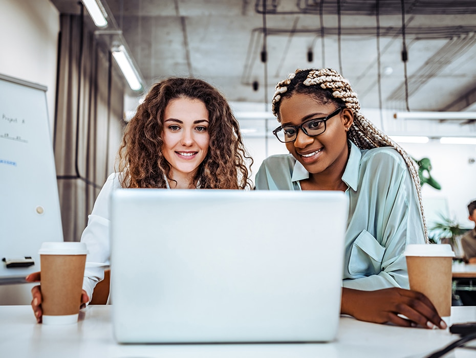 Two young women at a desk looking at something on a laptop