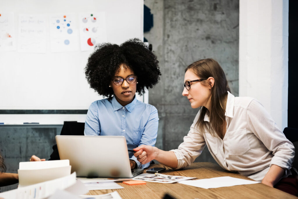 Two women working at a desk together reviewing something on a laptop